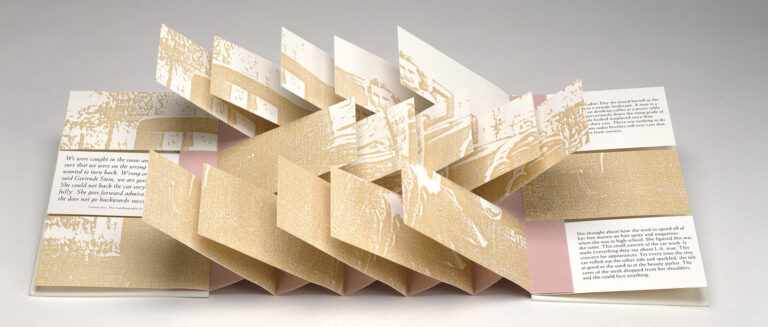 A pop-up book is open, displaying layered, accordion-style cutouts in beige and white, with printed text on the flat pages and abstract images on the folded pop-up sections. The background is plain and light gray.