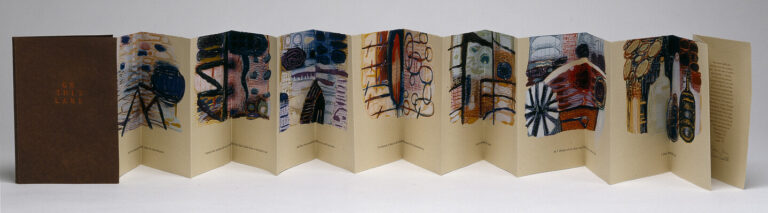 An accordion-style artist book with colorful abstract drawings and handwritten text on cream pages, displayed open in a zigzag shape. A brown cover stands at one end with the words "The Red Land" in gold.