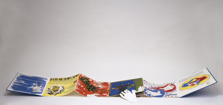 A colorful, accordion-style pop-up book is open on a white surface, displaying illustrated pages with text, festive images, and pop-up elements, including a white glove in the center.