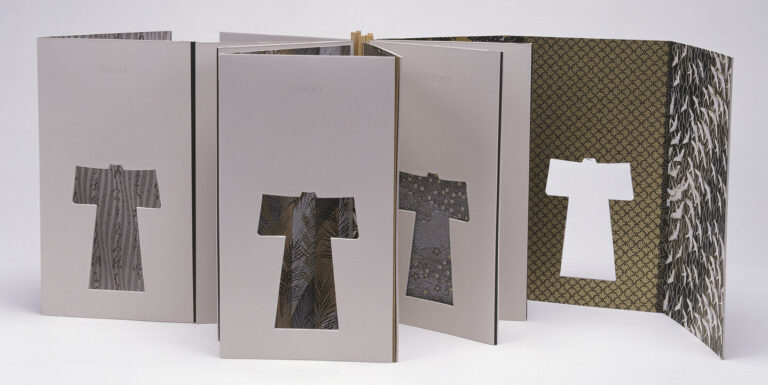 Several standing paper panels, each with a kimono-shaped cutout, are arranged in a row. Fabric or patterns show through the cutouts, and the background is plain white.