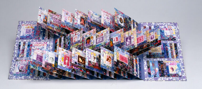 A colorful, intricate pop-up book is open, with multiple panels and pages standing upright, each featuring various images, patterns, and designs on a white background.