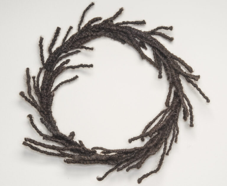A circular wreath made of dark, tightly coiled hair with strands escaping and resembling laurels.