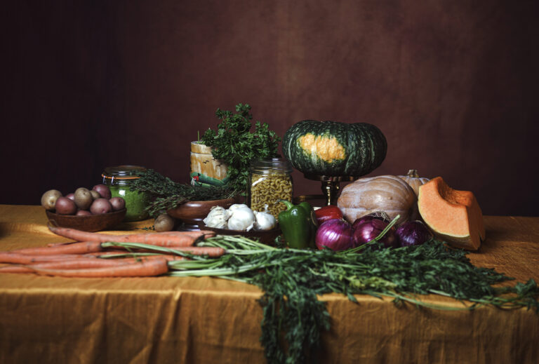 A photograph shows vegetables, including carrots, celery, peppers, onions, and squash, set atop a table with a golden yellow tablecloth.
