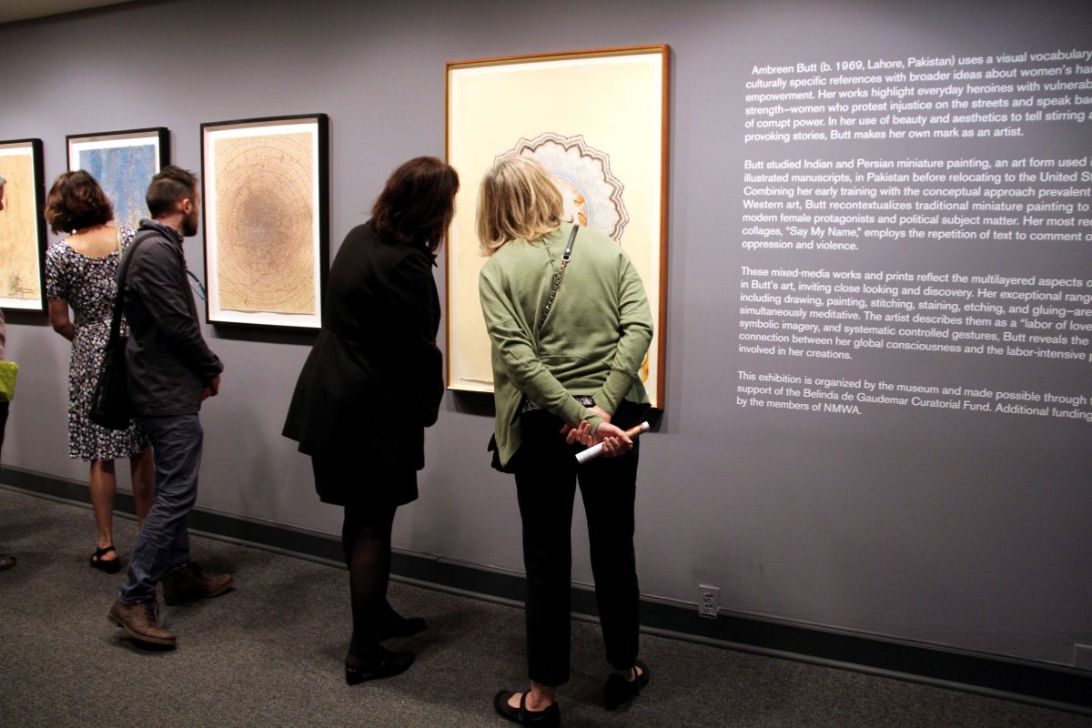 Museum visitors are studying art hanging on a dark wall.