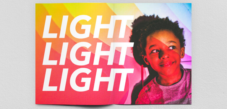 Open book with rainbow overlay features photograph of a child with medium-brown skin on the right side of the fold and the words "LIGHT LIGHT LIGHT" filling the page on the left.