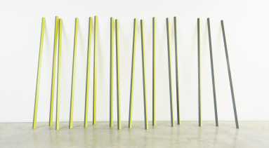 Sixteen rectangular yellow and grey aluminum poles lean up against a wall