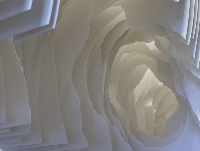 Detail view of torn sheets of white paper that can be looked through like a tunnel with pieces of paper blocking the view.
