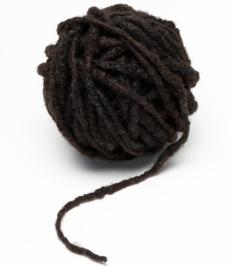 A sculpture of a skein of yarn, wound tightly into a ball, with a small tail extending on the end. The yarn is made of a long, dark, dreadlock.