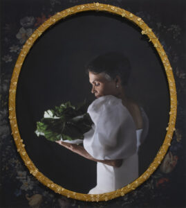 A photograph of an older Black woman with short grey hair in profile. She wears a long, white, gown with puffy sleeves. She holds and gazes at a head of collard greens.