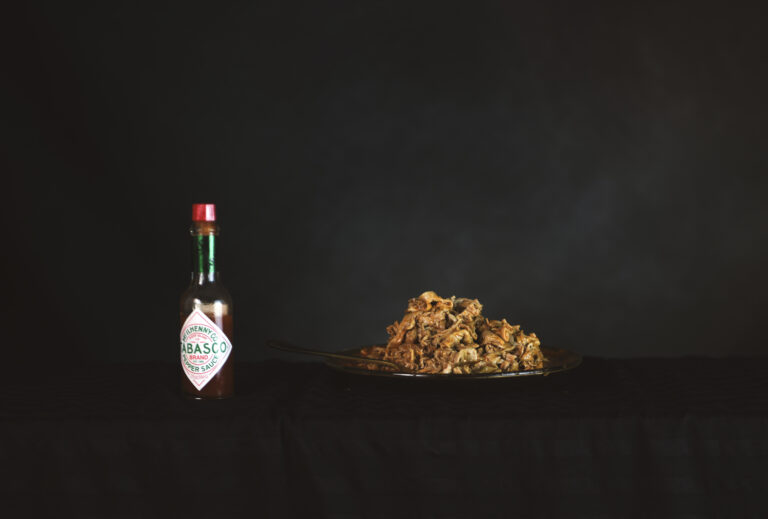 A photograph shows a bottle of Tabasco sauce and a plate of chitlins atop a black table.