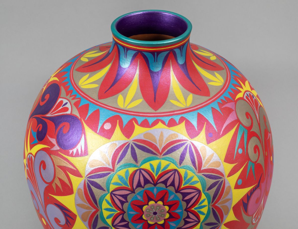 A round ceramic vase with a short neck decorated with intricate geometric and floral patterns painted in red, pink, blue, yellow, and purple.